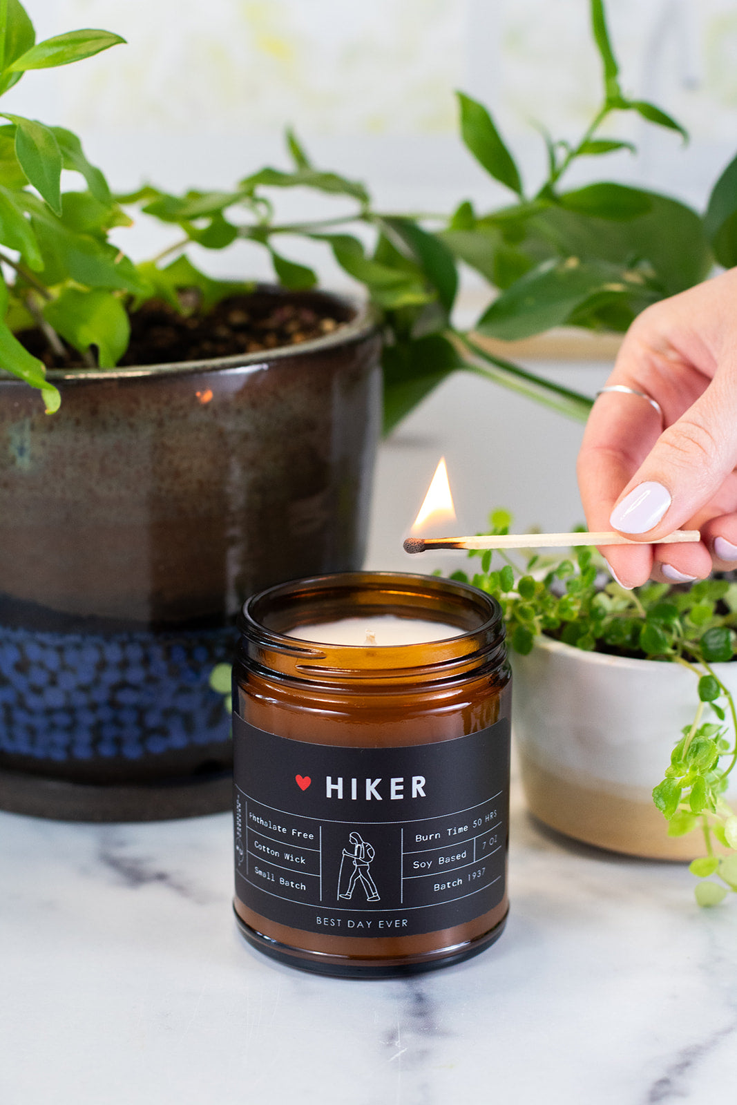 Hiker candle being lit with a match and with plants in background.